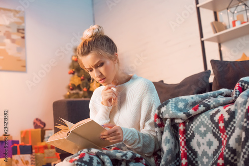 thughtful woman reading book at home on Christmas eve