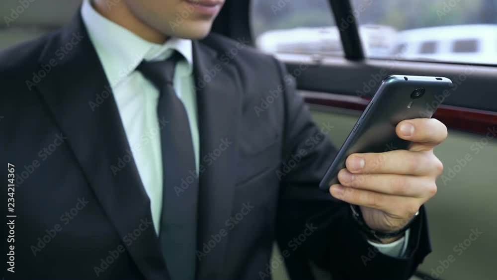 Young male boss using his smartphone while sitting in car, business meeting Young male boss using his smartphone while sitting in car, business meeting