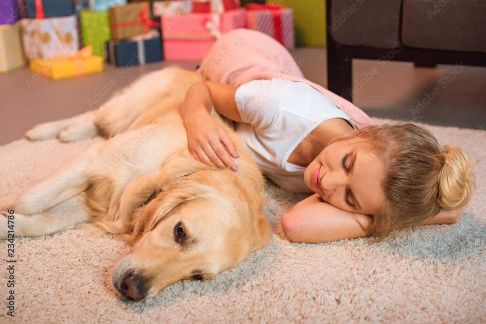 beautiful young blonde woman lying on floor and hugging golden retriever dog at home on fluffy rug at chistmas time beautiful young blonde woman lying on floor and hugging golden retriever dog at home on fluffy rug at chistmas time