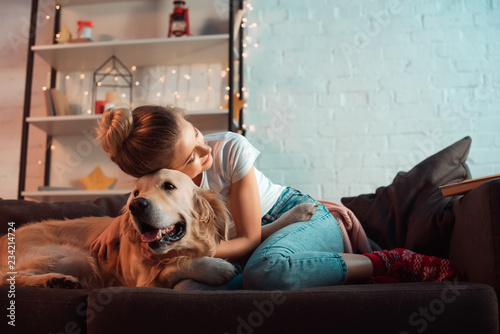 young blonde woman on couch hugging golden retriever dog at christmas time