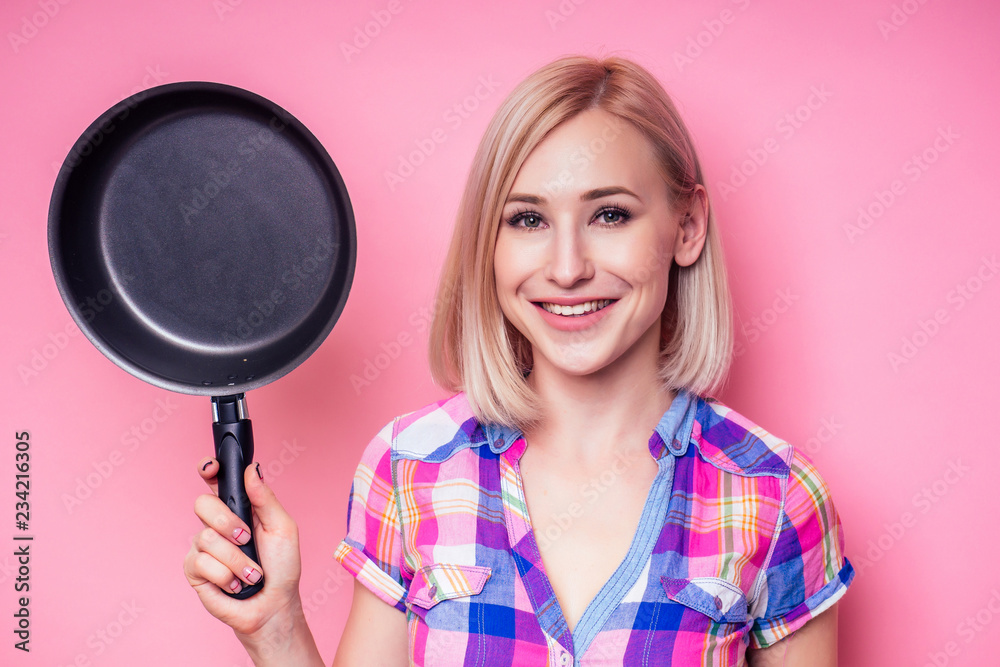 Beautiful blonde housewife woman holding pan on a pink background in the studio Beautiful blonde housewife woman holding pan on a pink background in the studio