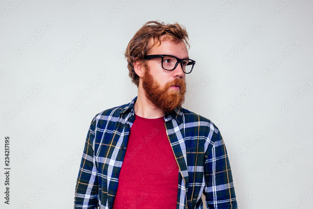 Close up portrait of redhead bearded male with red head and stylish glasses green tartan shirt and red cotton t-shirt on white background in studio. Close up portrait of redhead bearded male with red head and stylish glasses green tartan shirt and red cotton t-shirt on white background in studio.
