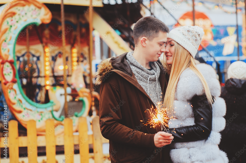 Obraz premium happy couple with christmas firelights walking in city holiday amusement park, carousel on background