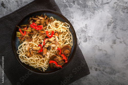 Traditional Asian food - noodles with seafood, salad, red pepper and fried mushrooms are on a gray table. Copy space. Top view
