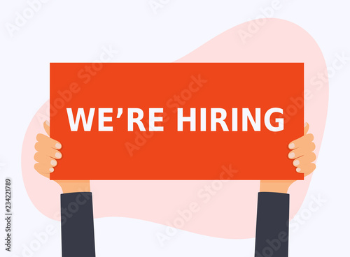 Hand holding the WE'RE HIRING banner. Business hiring and recruiting concept.