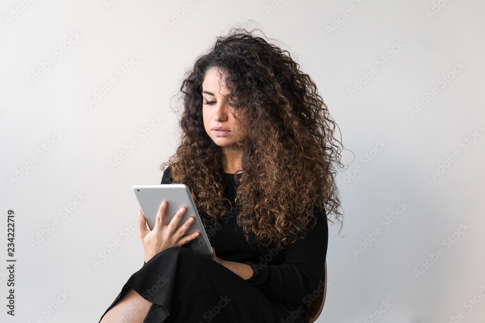 Beautiful woman with curly hair dressed on black working or shopping using computer or tablet Beautiful woman with curly hair dressed on black working or shopping using computer or tablet