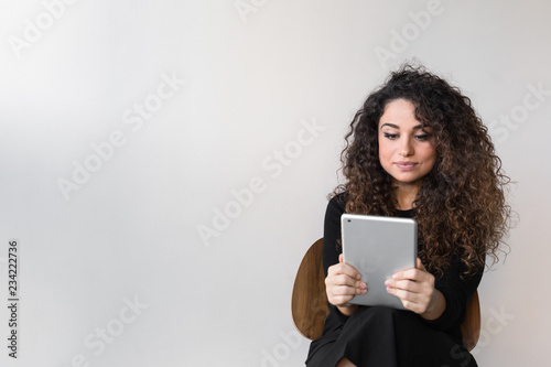 Beautiful woman with curly hair dressed on black working or shopping using computer or tablet