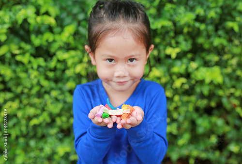 Asian child girl holding some thai sugar and fruit toffee with colorful paper wrapped in her hands. Focus at candy in her hands.