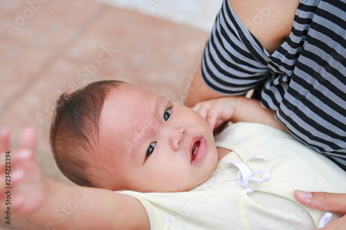 Close-up Asian baby boy lying in hug of mother with looking camera.