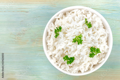 An overhead photo of a bowl of cooked white long grain rice, shot from above on a teal blue background with a place for text