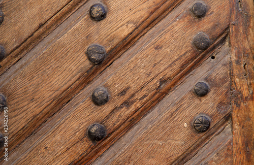 Background, texture. Image of an old wooden brown door surface with slats and nails. Cropped shot, close-up, nobody, vertical, abstraction. The concept of history and construction.