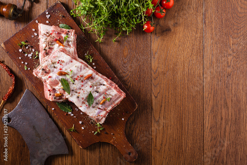 Raw pork ribs, on a plate sprinkled with spices.