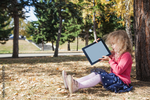 little girl playing with tablet outdoors near the trees, childhood and Technology