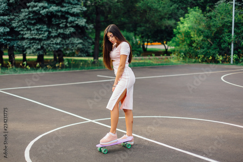 Portrait of a smiling charming brunette female standing on her skateboard on a basketball court.