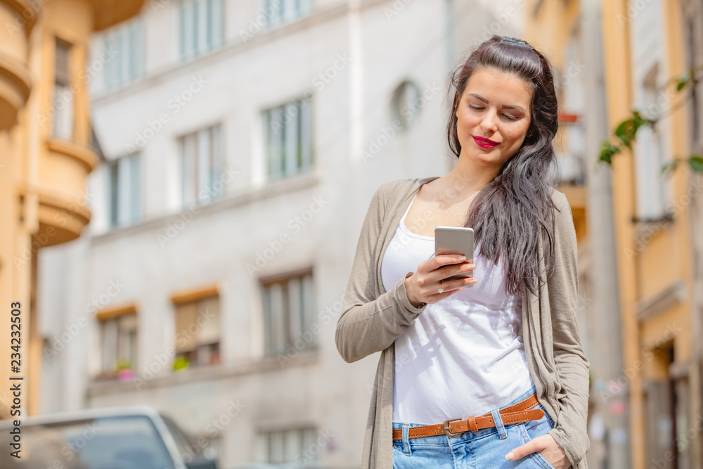 Cute young woman using cellphone in urban surroundings.