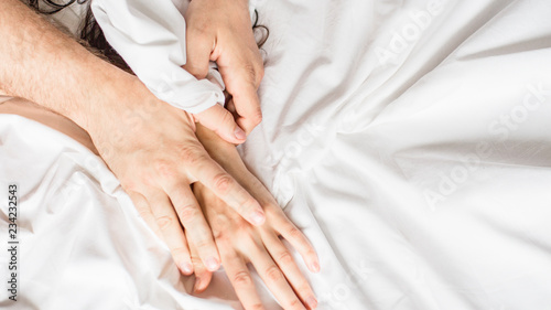 couples hold hands together in bed close-up touching each other on a white blanket. © Stavros
