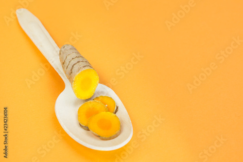 Sliced turmeric root on a wooden spoon, orange background photo