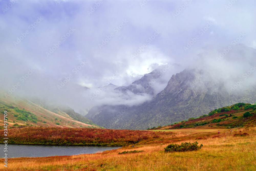 misty mountain valley with lush autumn vegetation and small lake, sheltered by low clouds