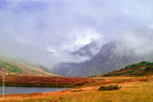 misty mountain valley with lush autumn vegetation and small lake  sheltered by low clouds