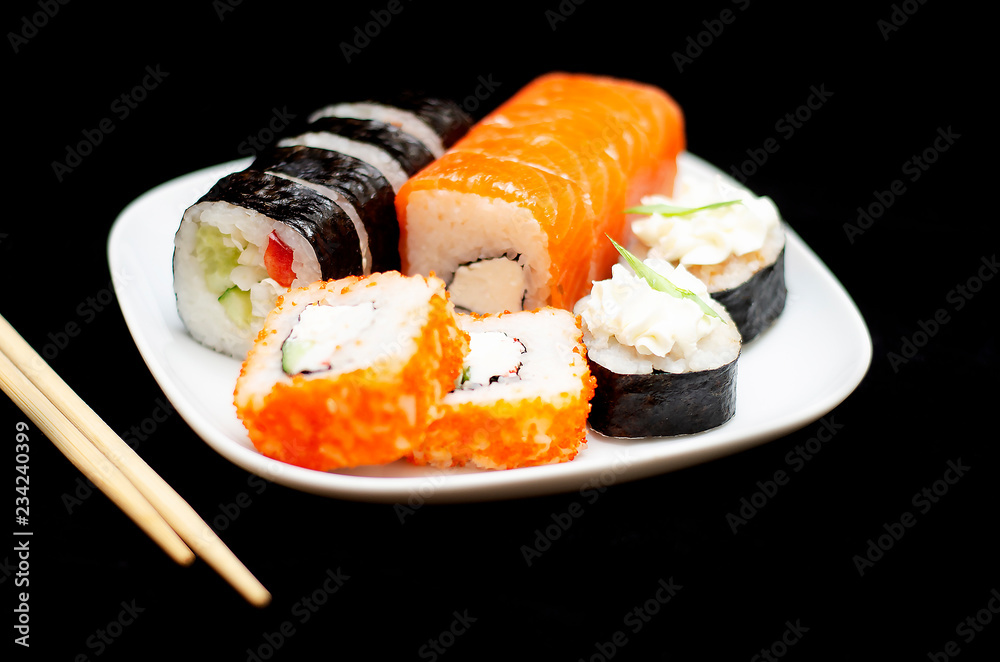 rolls with rice and fish on a white plate with wooden sticks on a black background rolls with rice and fish on a white plate with wooden sticks on a black background