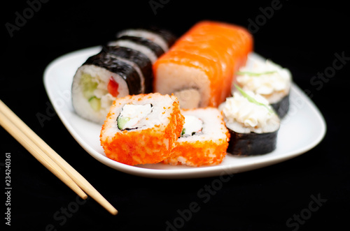 rolls with rice and fish on a white plate with wooden sticks on a black background