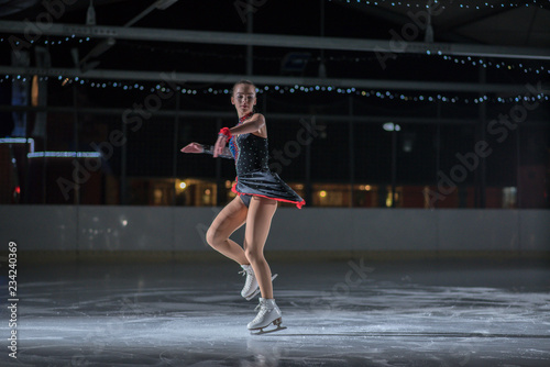 A beautiful ice skater is preparing to make a spin on the ice. She is hvaing a performance.