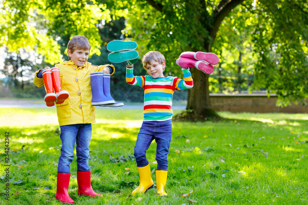 Two little kids boys, cute siblings with lots of colorful rain boots.  Children in different rubber boots and jackets. Footwear for rainy fall.  Healthy twins and best friends having fun outdoors Stock-Foto