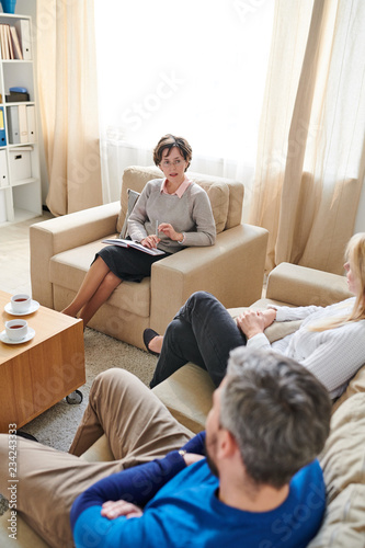 Obraz na plátně Serious confident qualified female therapist in skirt and sweater sitting in arm