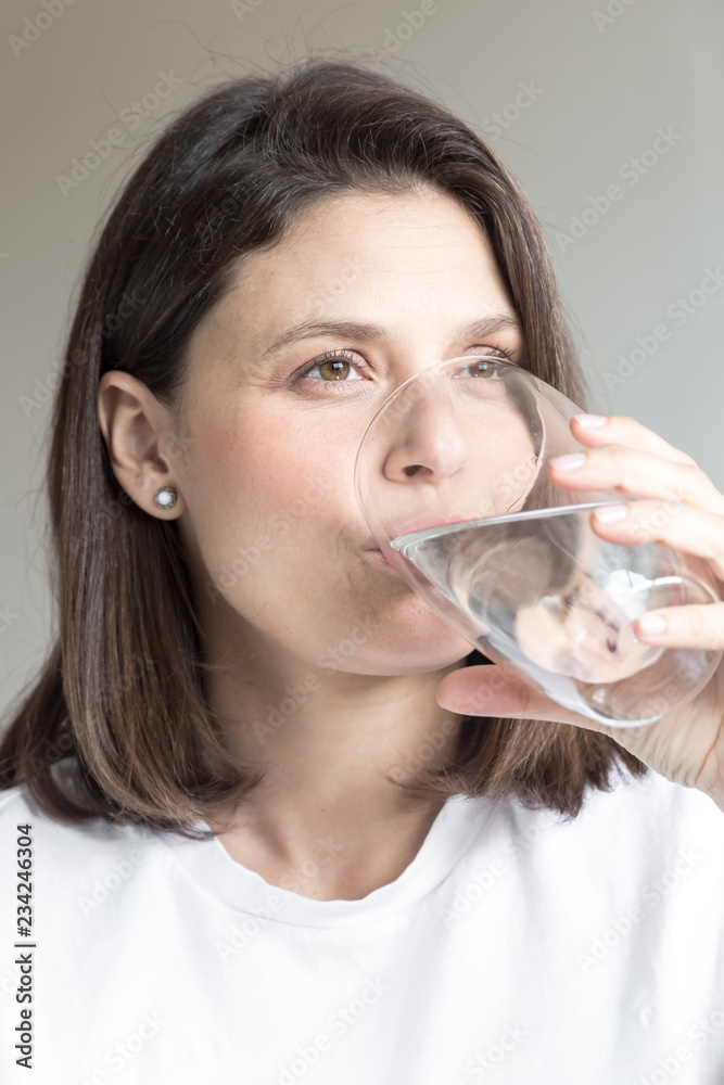Beautiful charming woman drinking a big glass of water and wearing white clothes Beautiful charming woman drinking a big glass of water and wearing white clothes