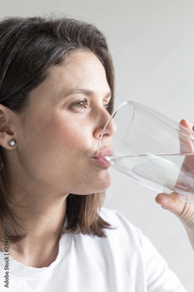 Beautiful charming woman drinking a big glass of water and wearing white clothes Beautiful charming woman drinking a big glass of water and wearing white clothes