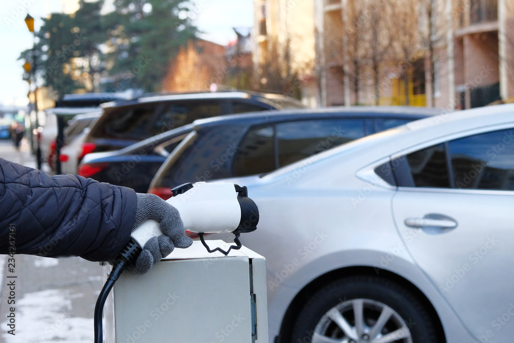Eco friendly transport concept. Car electric charger station installed in residential complex. Hand is holding charger for electric cars. Eco friendly transport concept. Car electric charger station installed in residential complex. Hand is holding charger for electric cars.