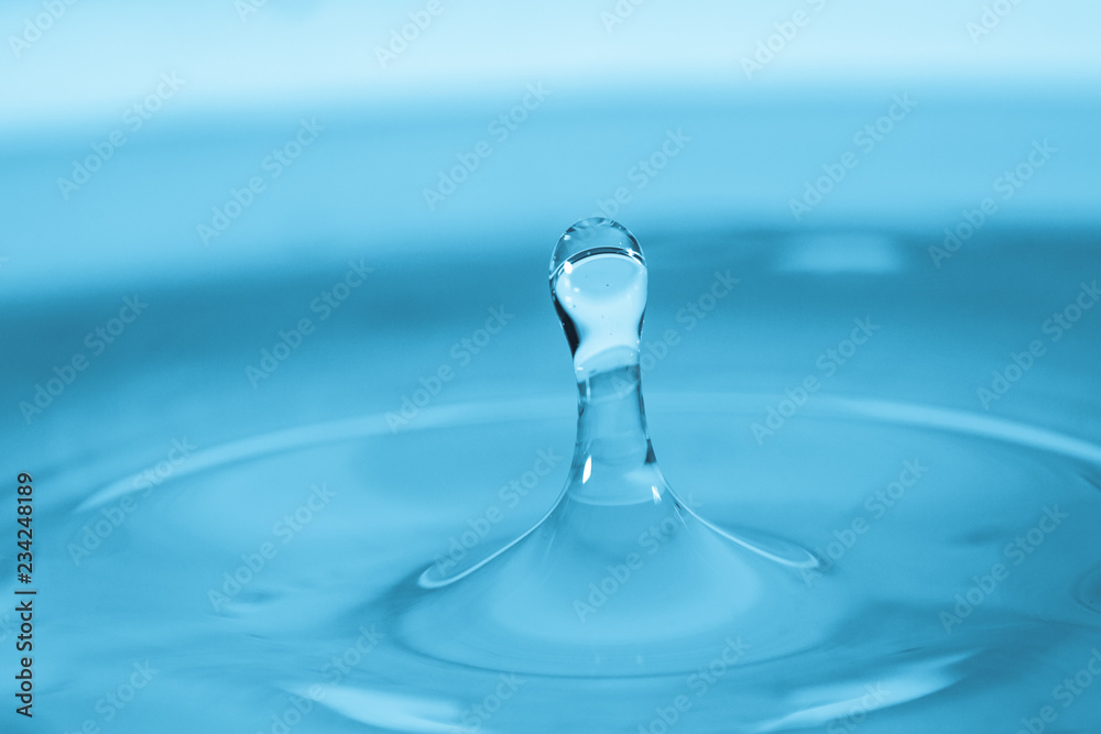 Water drop splash in a glass blue colored Water drop splash in a glass blue colored