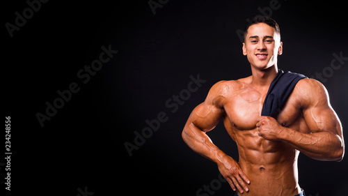 Strong bodybuilder man smiling with perfect abs, pecs, shoulders, biceps, triceps and chest holding a towel. Isolated on black background.