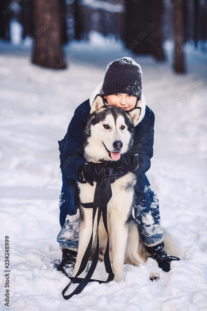 A cheerful European teenager hugs a big dog in the winter in the forest. The concept of winter holidays