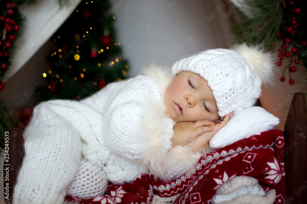 Adorable little toddler baby boy dressed in canta claus costume, sleeping in baby bed in front of Christmas teepee Adorable little toddler baby boy dressed in canta claus costume, sleeping in baby bed in front of Christmas teepee
