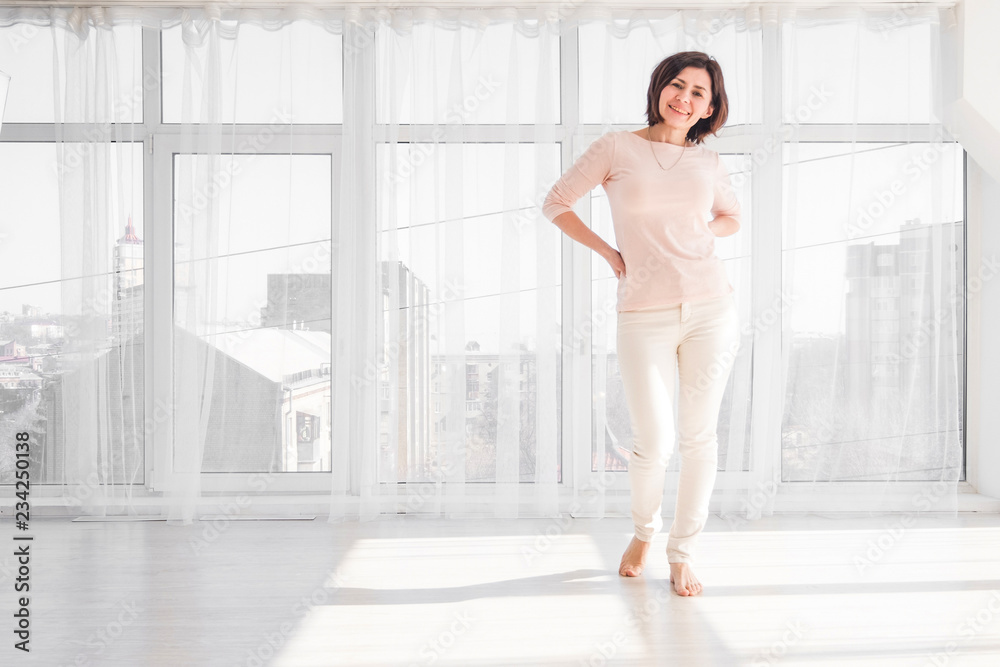 Beautiful stylish woman standing in a bright white room with large windows