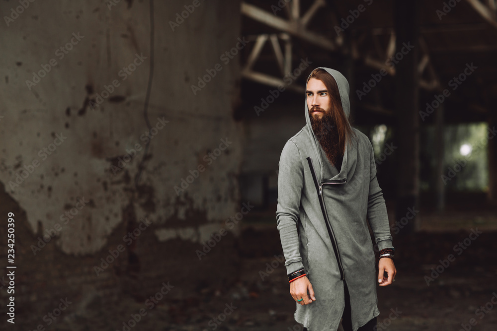 Young boy stands in an abandoned building. Wandering boy.The guy is dressed in stylish clothes, he has a long beard.