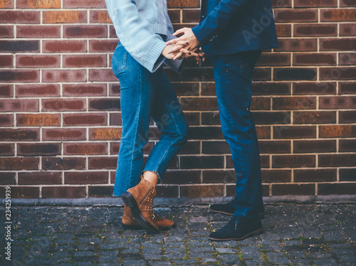 Stylish couple holding hands near brick wall
