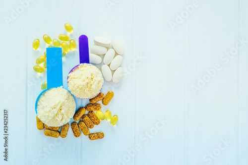 Closeup blue and purple measure dishes with protein powder and white-yellow sport pills around, top view