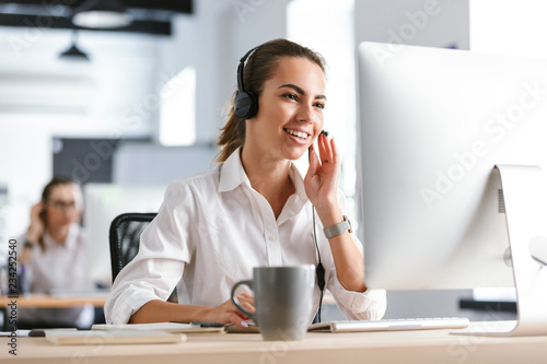Emotional business woman in office callcenter working with computer wearing headphones. photo