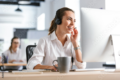 Emotional business woman in office callcenter working with computer wearing headphones. photo