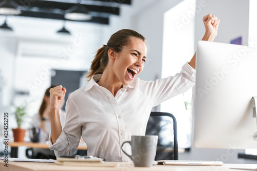 Photos Happy excited business woman in office working with computer make winner gesture