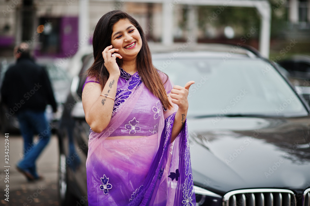 © AS Photo Family - Indian hindu girl at traditional violet saree posed at street against black business suv car and speaking on mobile phone, shows thumb up. © AS Photo Family - Indian hindu girl at traditional violet saree posed at street against black business suv car and speaking on mobile phone, shows thumb up.