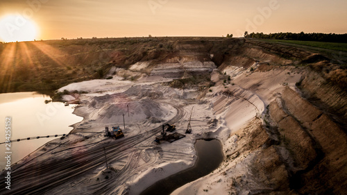 Aerial view of sandy quarry surface and mine equipment near lake at evening sunset