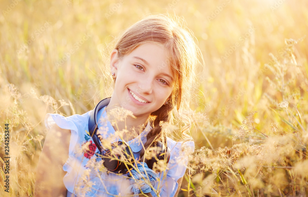 Smilling teenage girl with headphones on sunshine field background Smilling teenage girl with headphones on sunshine field background