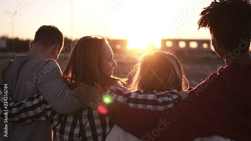 Group of friends walking embracing and having fun together in city. They are two girls and two boys in their twenties, friendship and lifestyle concepts, autumn clothing. Sun strongly shining on the photo