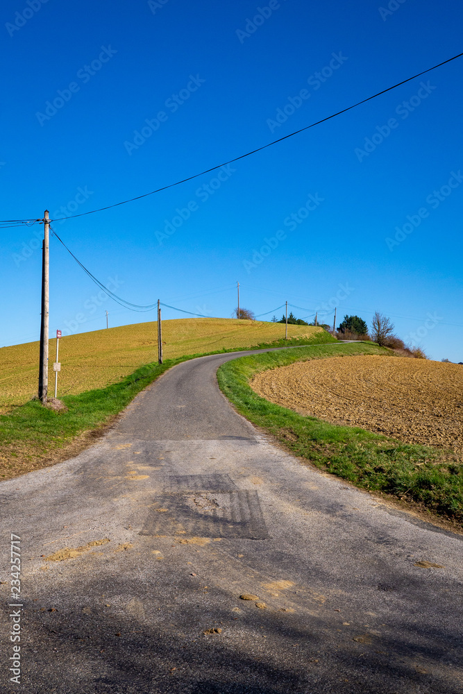 Petite route avec virage sur coline, champs labourés, automne, Occitanie, France