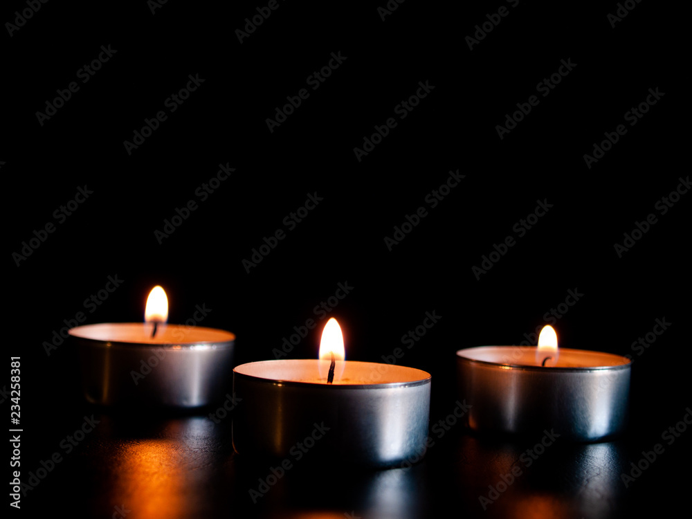 Three lighted candles with an orange flame and isolated on a black background Three lighted candles with an orange flame and isolated on a black background