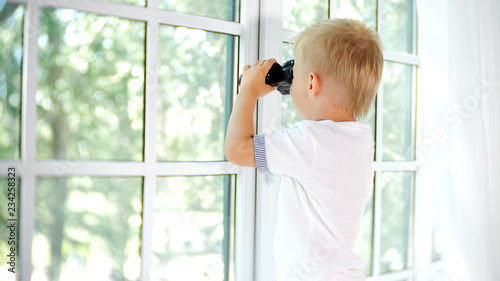 Little curious boy looking in window with binocular