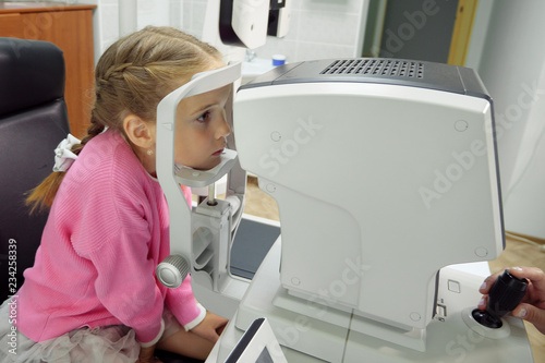 Close up of woman doctor working with the refractometer machine. A little girl having her eyes tested
